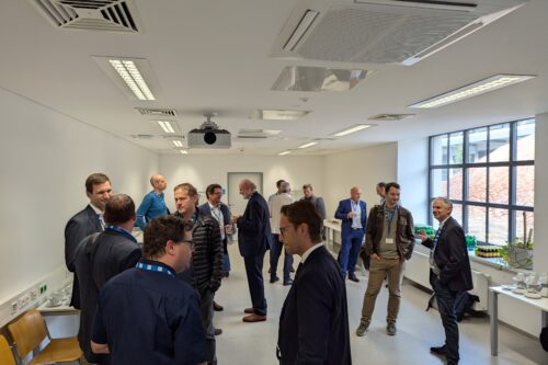 Mehrere Personen stehen in einem hellen Raum und unterhalten sich in kleinen Gruppen während einer Veranstaltung.