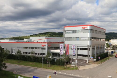 Exterior view of a modern igm company building with production halls, office areas, and flags in front of the entrance.