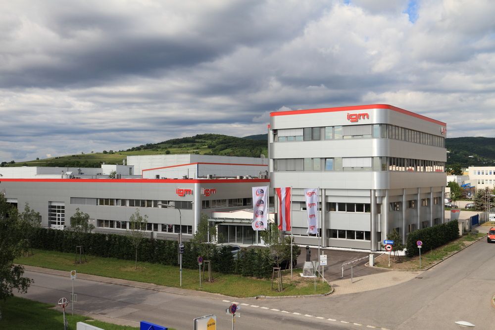 Exterior view of a modern igm company building with production halls, office areas, and flags in front of the entrance.
