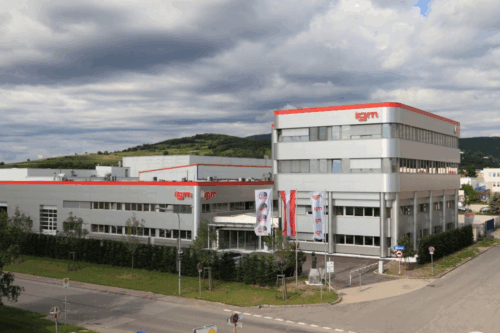Exterior view of a modern igm company building with production halls, office areas, and flags in front of the entrance.